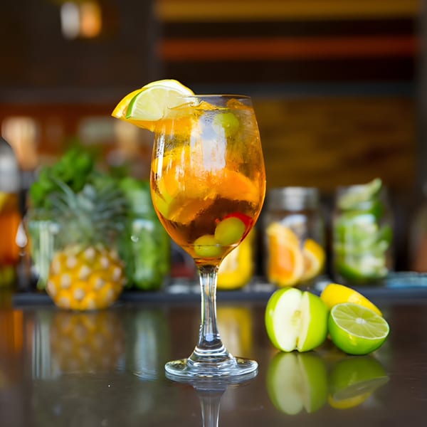 Aro Latin's sangria in a wine glass, garnished with lime, with fruit and pineapples in the background.
