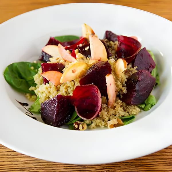 Aro Latin's quinoa salad with beets, apples, spinach, and nuts on a white plate.