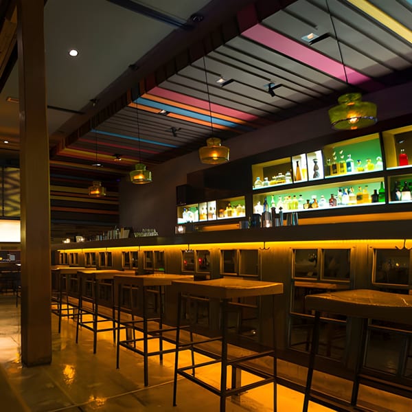Aro Latin's bar area with high-top tables, stools, and a colorful ceiling, illuminated by warm lighting.