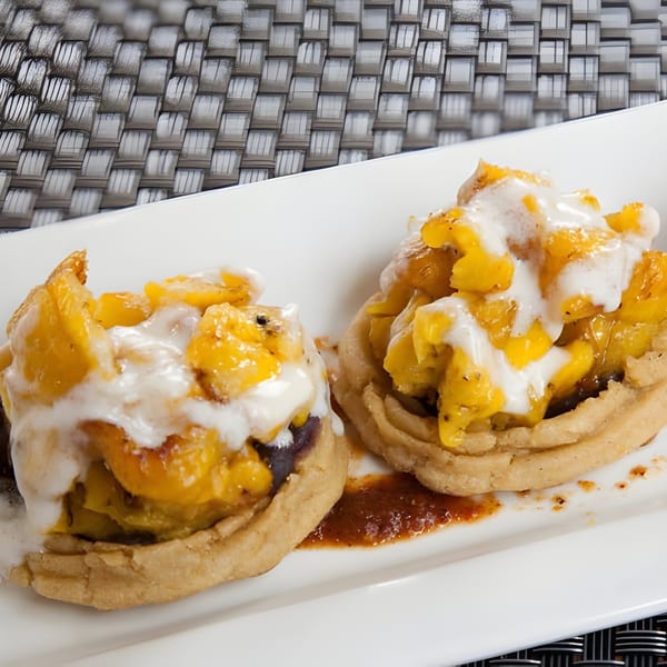 Two Aro Latin sopes topped with plantains, black beans, and crema on a white plate.