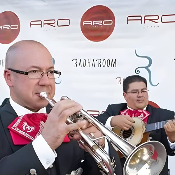 Two mariachi musicians, one playing a trumpet and the other a guitar, performing at Aro Latin.