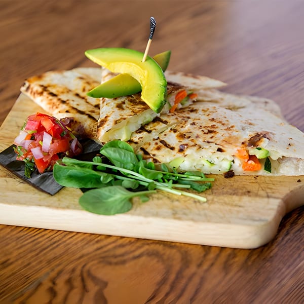 Grilled Aro Latin quesadillas with avocado, pico de gallo, and fresh greens on a wooden board.