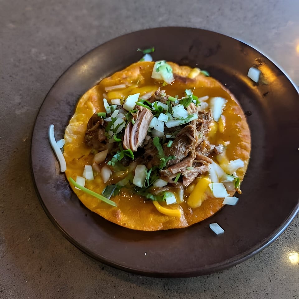 Aro Latin's carnitas tostada with shredded pork, diced onions, and cilantro on a dark plate.