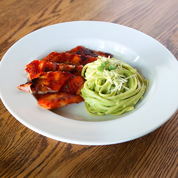 Aro Latin's grilled chicken with red sauce and green pasta topped with cheese and microgreens.