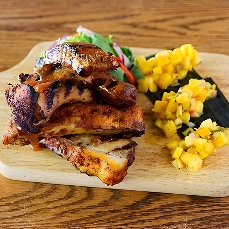 Grilled pork belly slices with mango salsa and a side salad on a wooden cutting board.