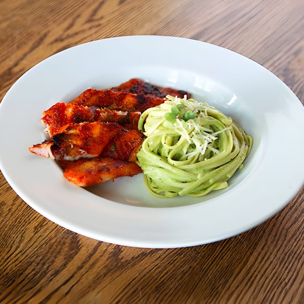 Aro Latin's grilled chicken with red sauce and green pasta topped with cheese and microgreens.