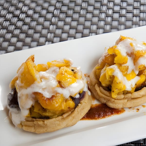 Two Aro Latin sopes topped with yellow plantains and white crema on a white plate.